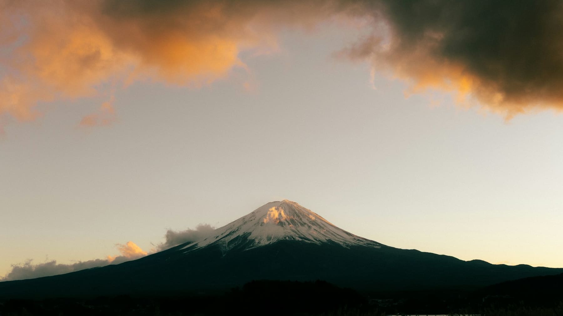 Snow-capped Mount Fuji under orange-lit clouds