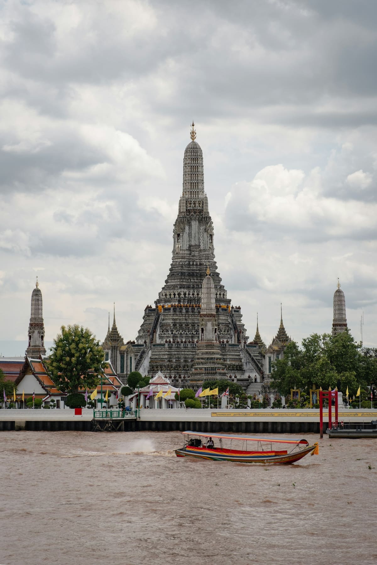 Wat Arun temple on the Chao Phraya river in Bangkok, with a long-tail boat passing