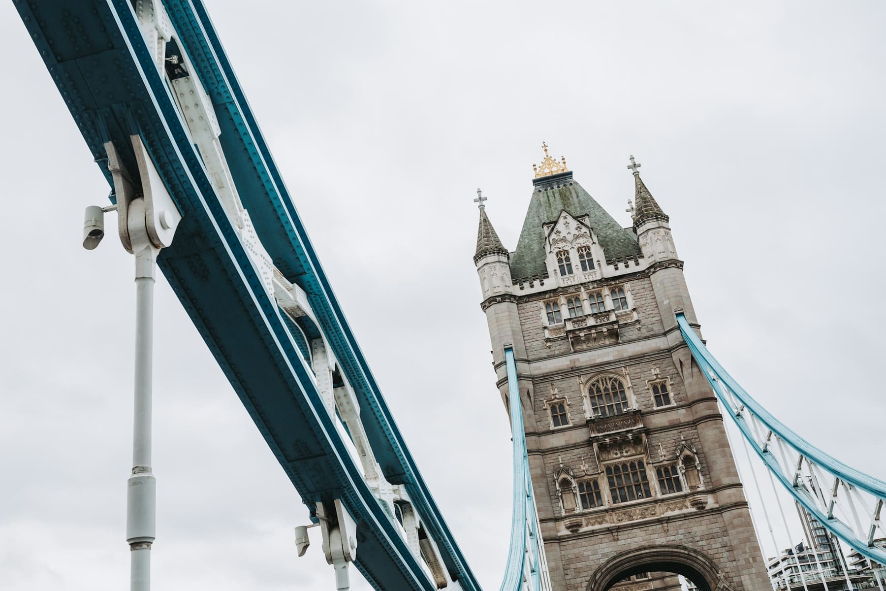 Looking up at a tower of Tower Bridge in London and its blue suspension chains